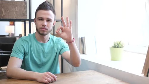 Young Man Gives OK Sign at Table