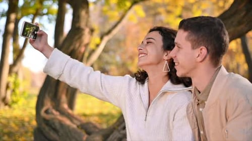 A romantic couple in an autumn park. Smiling and taking selfies. Autumn atmosphere, yellowed trees a