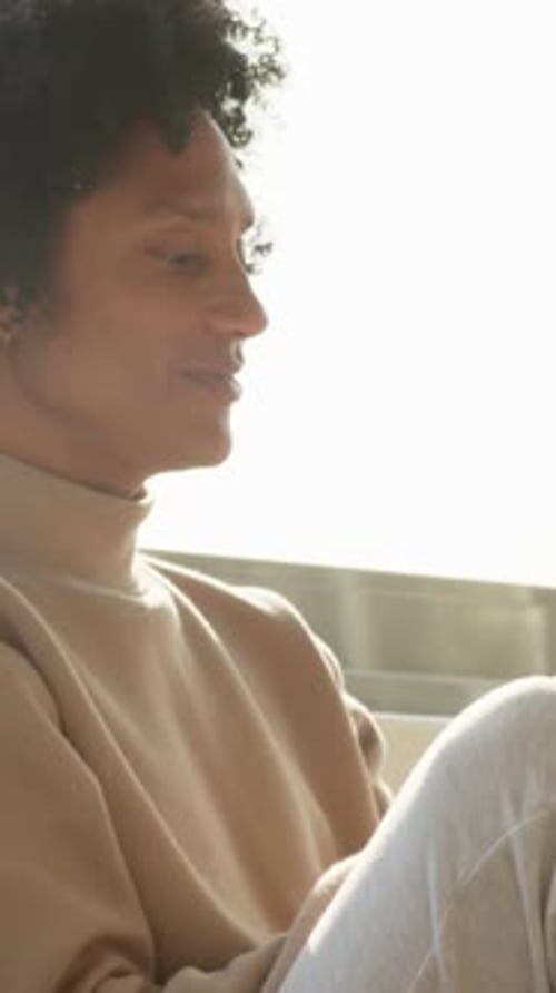 Vidéo verticale : lumière de fenêtre dessinant un homme en pull beige baissant le regard vers la maison, pensant, boucle d'oreille