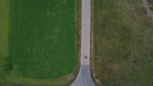Aerial drone shot of motorcyclist driving down a small farm road.