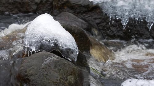 isolated icy rock in natural stream of water, slow motion