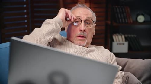 Senior Man Rubbing Eyes in Front of Laptop