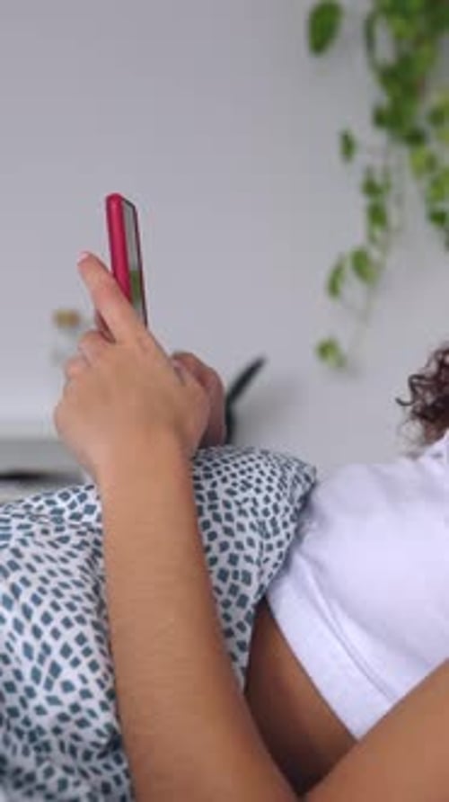 Young Woman Using Mobile Phone Resting on Bed in the Morning