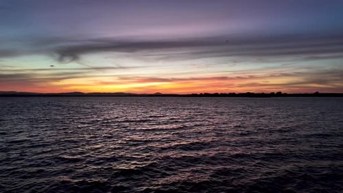 Die untergehende Sonne wirft ein orangefarbenes Leuchten auf das Wasser und schafft eine wunderschöne und dramatisch Szene