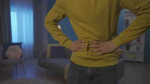 A Man is in Pain While Standing in the Living Room Hands of a Man Holding Kneading His Stomach Close