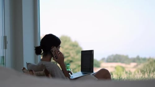 Woman in relaxed attire working from home using laptop and smartphone. Home office