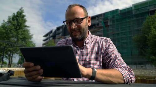 Young man browsing internet on tablet computer relaxing in city park