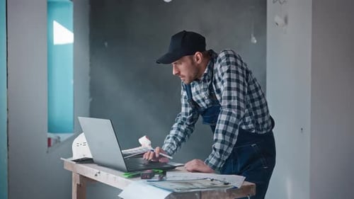 A Male Contractor Builder at a Construction Site Working with a Project on a Laptop An Engineer is
