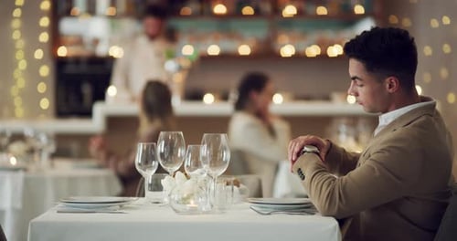 A young man looking at his watch while waiting for someone at a restaurant
