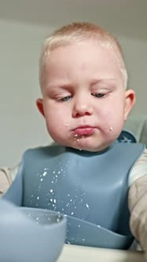Blonde infant eating with a spoon and bib