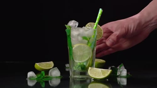 Close-up of the bartender's hand picking up a glass of Mojito from the table