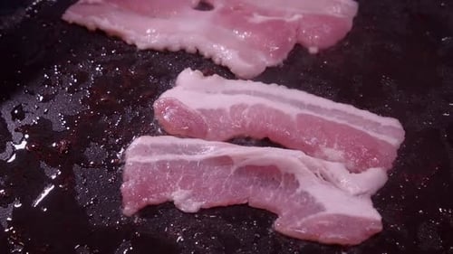 Fast motion closeup: Slices of fatty bacon shrink as they cook in pan
