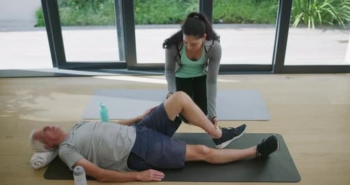 Senior Man Exercises Leg with Young Woman