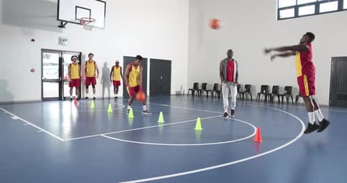 Basketball players practicing dribbling skills in gym with coach observing