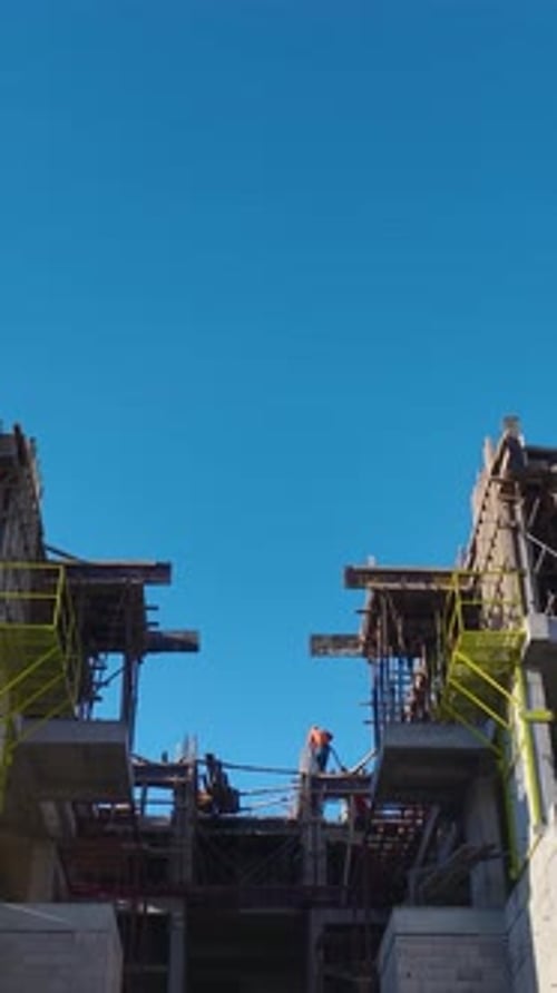 Vertical Video of a House Under Construction With Workers Placing Steel Frames and Pouring Cement