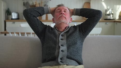 Senior Man Stretching Neck on Sofa Indoors