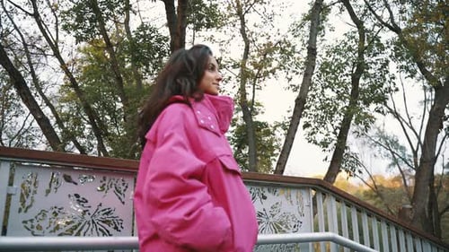 Pretty Young Female Wearing Stylish Pink Jacket and Going Down Stairs While Walking in the Park