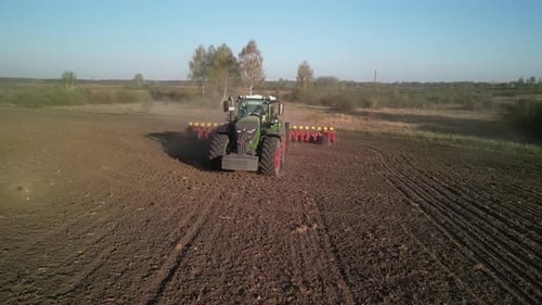Green tractor works on the field sowing sunflower. Tractor planting corn in Ukraine
