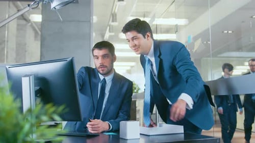 In the Office Businessman Sitting at His Desk Talks with His Colleague, they're pointing at Compute