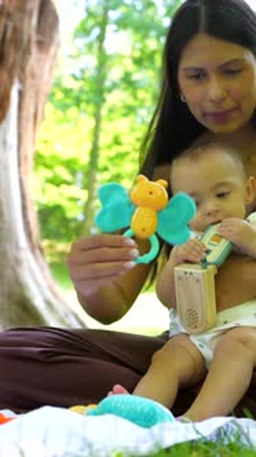 Latin Mother Entertaining Baby Girl with Toys in Park
