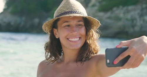 Beautiful young girl doing selfie at the sea, smiling waving at the camera, in a swimsuit in a str