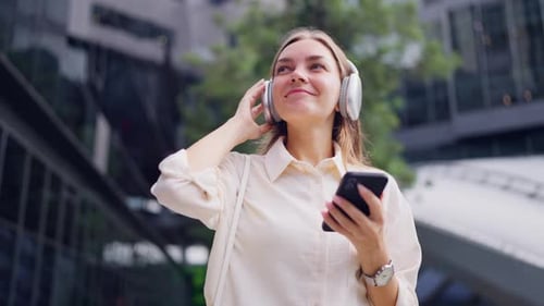 Caucasian businesswoman listen music on headphones outside the office.