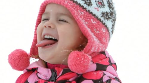 Joven feliz con abrigo de invierno y bufanda come juguetonamente copos de nieve al aire libre