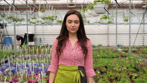 Young Woman Standing in a Flower-Filled Greenhouse