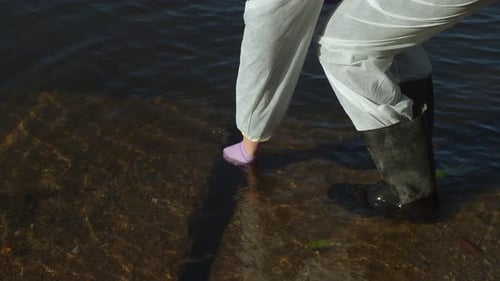 Water sampling from river into test tube, woman in protective suit, middle shot
