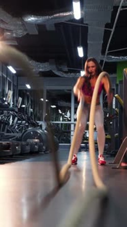 Front view of a happy healthy female doing exercises with the ropes in the gym.