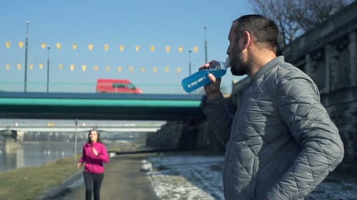 Male Jogger Drinking Isotonic Drink And Woman Running In City