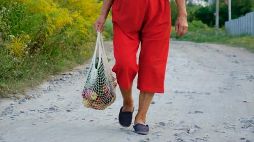 Senior Woman Walking on Rural Road with Groceries