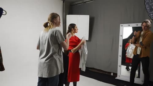 Model and Production Team in the Studio Female Model and Girl Assistant Picking Clothes for Scene