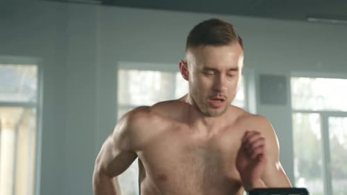 Man Sweating, Running on Treadmill in Bright Gym