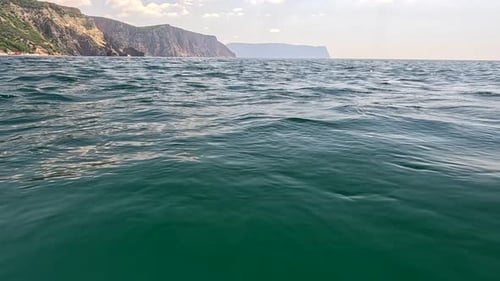 Sea Water Surface Camera Flies Over the Calm Azure Sea with Volcanic Rocky Shores on Background