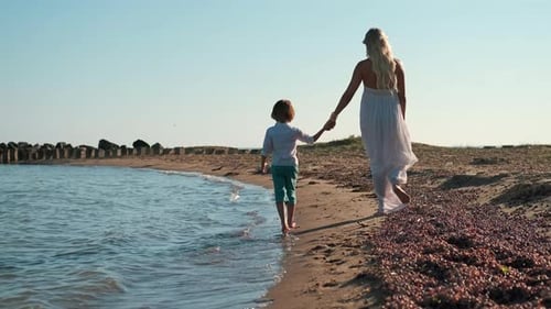 Woman and Child Walking Together on Beach Holding Hands