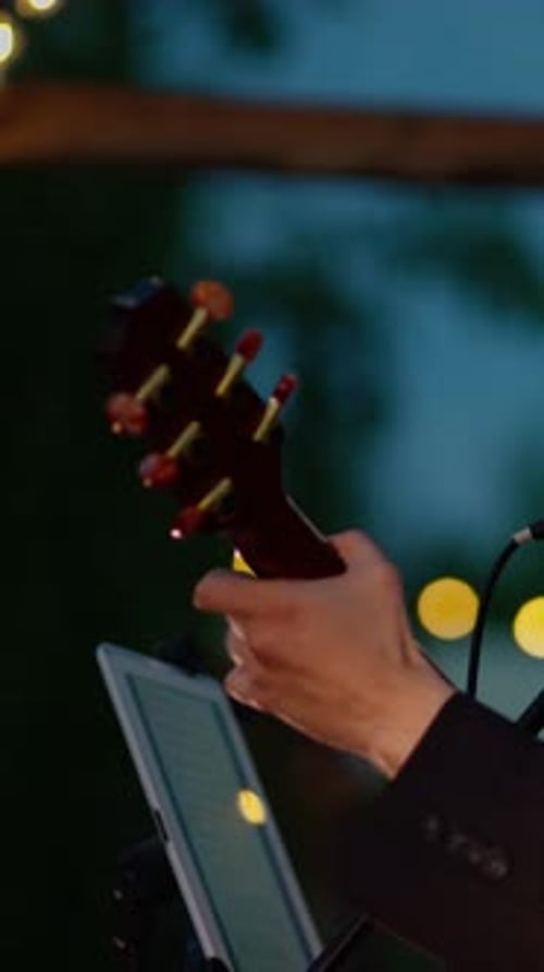 Closeup of Guitarist Hands on Acoustic Headstock with Warm String Lights Bokeh
