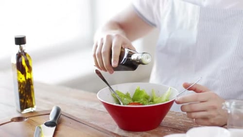 Man mixing fresh salad ingredients in a bowl preparing a healthy meal at home