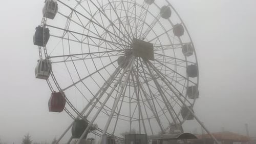 Lowangle View From Ground of Ferris Wheel Rotation Against Gray Gloomy Cloudy Sky in Rainy Autumn