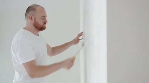 Nahaufnahme eines jungen Mannes malt die Wand mit einer Rolle mit weißer Farbe