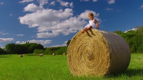 Attractive Little Girl in a White Dress on a Haystack Enjoys Freedom