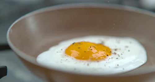 Chef Seasons a Frying Egg, Sunny Side Up, with Ground Pepper In