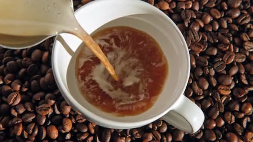 Creamy Coffee Poured into Mug on Coffee Beans
