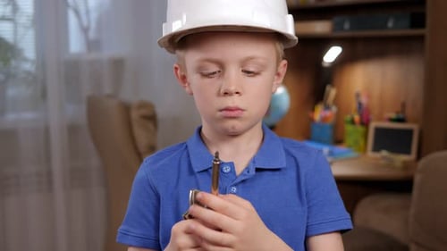 Portrait of a Boy in a White Helmet with Various Tools in His Hands at Home