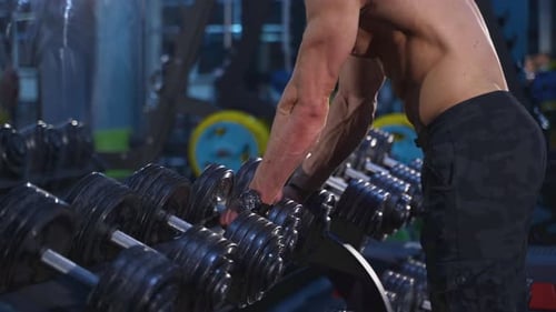 Young man with naked torso taking weight. Handsome bodybuilder working with huge weight.