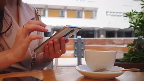 Business Hands with a Woman in a Cafe Sitting at a Table and Typing a Message on Her Smartphone and