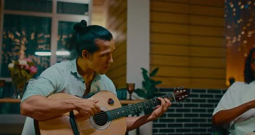 Man Plays Guitar and Sings with Friend Indoors