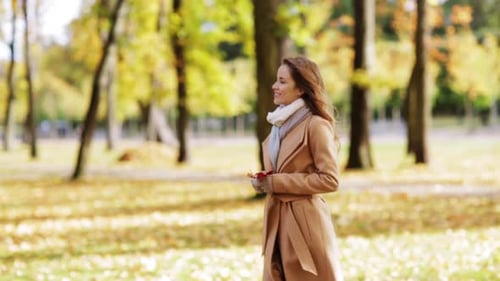 Beautiful young woman enjoys autumn day walking in park with maple leaf