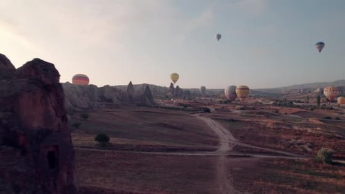 Drone flies through rock opening, revealing Cappadocia's balloons