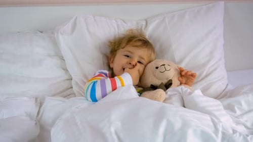Child Lies in Bed with Teddy Bear